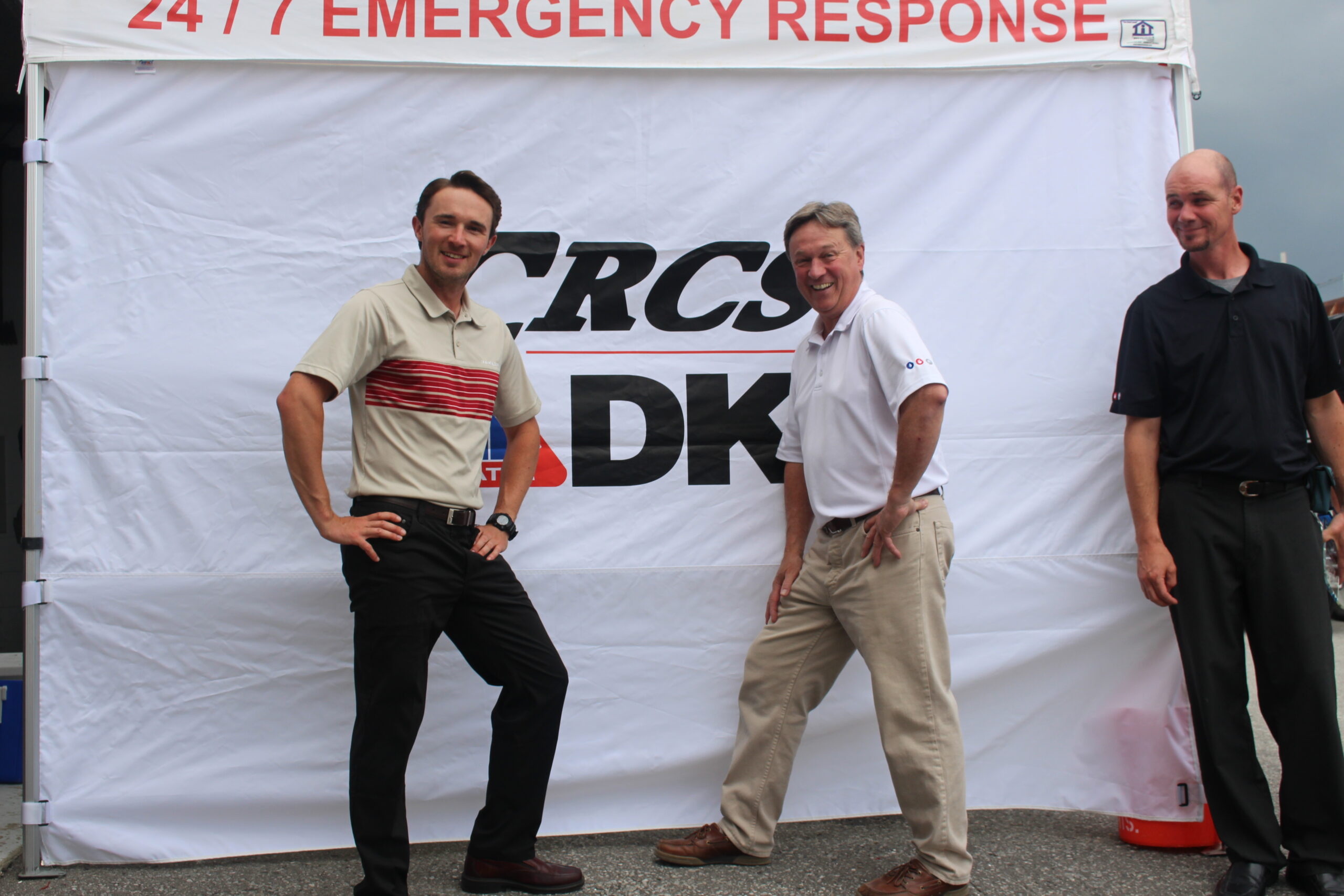 Two men pose with their arms on their hips smiling as they stand in front of the DKI-CRCS white banner.